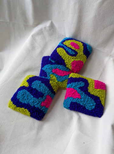 This is an image of four punch needle coasters featuring an abstract freeform design of blobs and curves in hot pink, acid green, deep indigo, and teal blue. Bright Set of Coasters / Mini Rugs by dancing arms in Los Angeles, California.