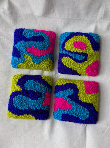 This is an image of four punch needle coasters featuring an abstract freeform design of blobs and curves in hot pink, acid green, deep indigo, and teal blue. Bright Set of Coasters / Mini Rugs by dancing arms in Los Angeles, California.