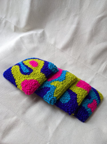 This is an image of four punch needle coasters featuring an abstract freeform design of blobs and curves in hot pink, acid green, deep indigo, and teal blue. Bright Set of Coasters / Mini Rugs by dancing arms in Los Angeles, California.