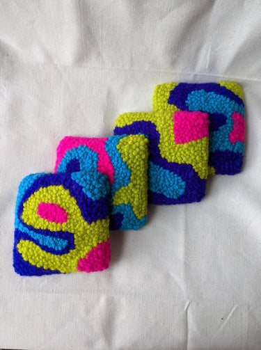 This is an image of four punch needle coasters featuring an abstract freeform design of blobs and curves in hot pink, acid green, deep indigo, and teal blue. Bright Set of Coasters / Mini Rugs by dancing arms in Los Angeles, California.
