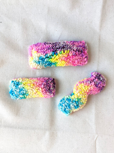 This is an image of a squiggle shaped punch needle hair barrettes made with a rainbow yarn. Dancing arms punch needle hair accessories.