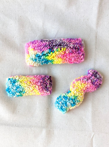 This is an image of a small sized punch needle hair barrettes made with a rainbow yarn. Dancing arms punch needle hair accessories.