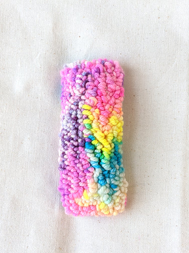 This is an image of a medium sized punch needle hair barrettes made with a rainbow yarn. Dancing arms punch needle hair accessories.