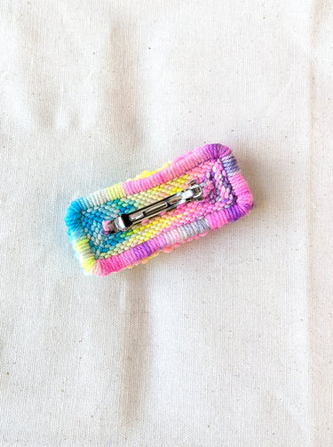 This is an image of a small sized punch needle hair barrettes made with a rainbow yarn. Dancing arms punch needle hair accessories.