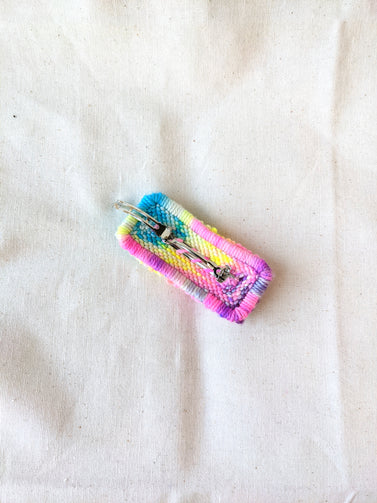 This is an image of a small sized punch needle hair barrettes made with a rainbow yarn. Dancing arms punch needle hair accessories.