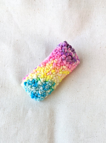 This is an image of a small sized punch needle hair barrettes made with a rainbow yarn. Dancing arms punch needle hair accessories.