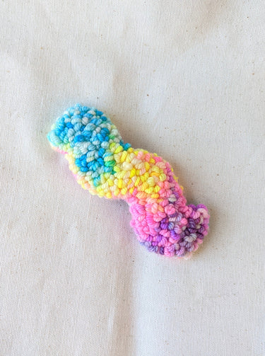 This is an image of a squiggle shaped punch needle hair barrettes made with a rainbow yarn. Dancing arms punch needle hair accessories.