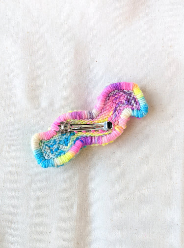 This is an image of a squiggle shaped punch needle hair barrettes made with a rainbow yarn. Dancing arms punch needle hair accessories.