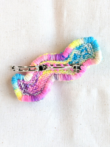 This is an image of a squiggle shaped punch needle hair barrettes made with a rainbow yarn. Dancing arms punch needle hair accessories.
