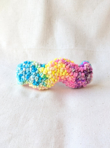 This is an image of a squiggle shaped punch needle hair barrettes made with a rainbow yarn. Dancing arms punch needle hair accessories.